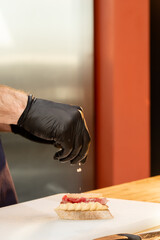 close-up of a chef's hand pouring salt onto prepared meat salt and cheese paste sandwich