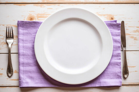 Light violet linen on rustic white slat wood surface, small white plate, knife and fork, shot overhead, top view. Food or dessert presentation background, banner, empty, template, backdrop.