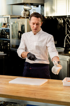 a chef in a white jacket in the kitchen wearing black gloves wipes a knife with a white towel