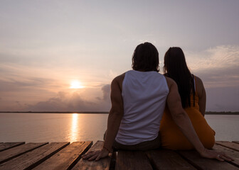 pareja sentada de espaldas en un muelle viendo el amanecer en laguna de bacalar