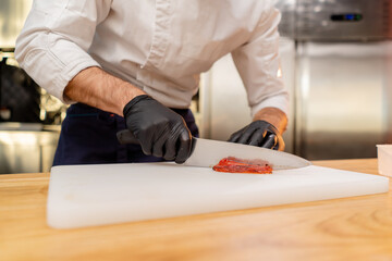 Obraz na płótnie Canvas close-up of the hands of chef in a white jacket wearing black gloves slicing bell peppers
