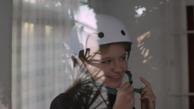 A beautiful blonde puts a white bicycle helmet on her head. The video was shot through the window.