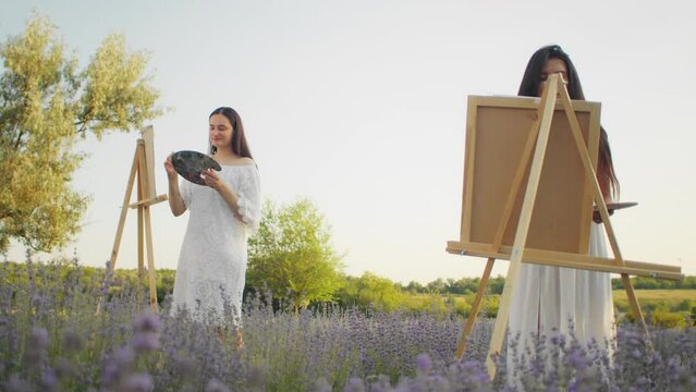 Two women painting on canvases in a lavender field at dusk. Artistic activity and creativity in a natural setting concept for design and print with place for text.