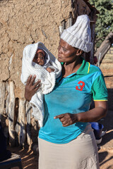 village african woman holding a baby, mud house in the background