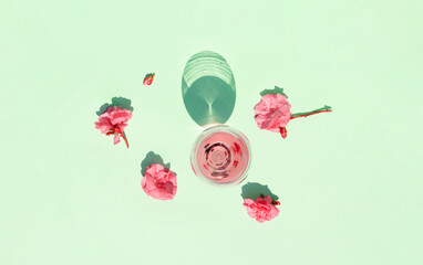 Minimal scene with pink oleander flowers and glass of red wine on sunny day and pastel green...