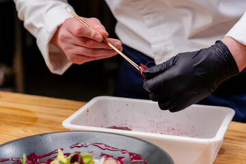 close-up of black plate in which salad the chef's hands add pieces of beet to it with tweezers