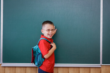 A Happy child child standing at the blackboard with a school backpack wearing glasses