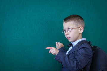 A Happy child child standing at the blackboard with a school backpack wearing glasses