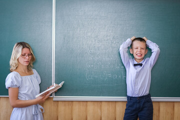 A Happy child child standing at the blackboard with the school teacher at the lesson