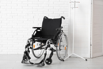 Empty wheelchair with stand for IV drip near white brick wall