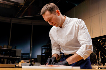 a chef in a white jacket in a professional kitchen cuts fish with knife before cooking