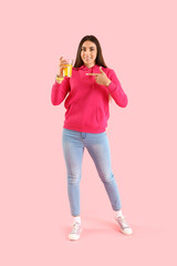 Young woman pointing at glass of juice on pink background