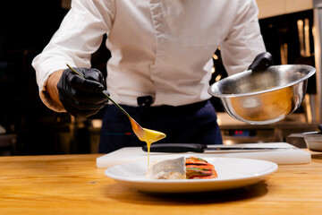 close-up of a chef's hands holding a bowl and pouring sauce from a spoon onto the finished dish
