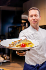 the chef demonstrates a ready-made fish dish at arm's length in professional kitchen