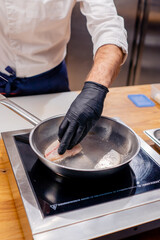 close-up of a chef's hands trying to turn fish fillet on a hot frying pan