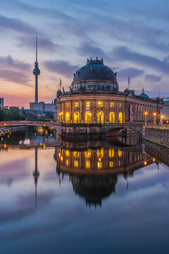 Museum Island in Berlin in the morning. Illuminated buildings and the television tower just before sunrise. Reflections on the water surface from the river Spree and clouds in the sky