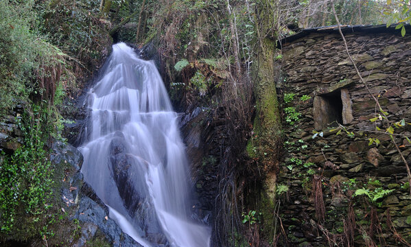 Waterfall next to a ruin of a mill built on the side of a mountain