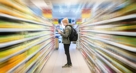 Customer choose food items on supermarket shelves in grocery store. Market shelves in blurred motion effect. - obrazy, fototapety, plakaty