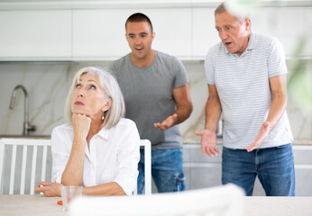 Elderly man and adult man during family quarrel with elderly woman in kitchen