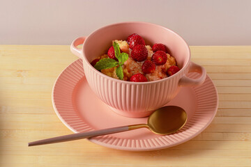 Wheat porridge in pink soup bowl. Grain porridge. Healthy breakfast. Wheat porridge with cream. Fresh strawberries and lemon balm leaves to decorate dish
