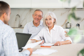 Couple of elderly man and woman discussing deal with male salesman in kitchen home