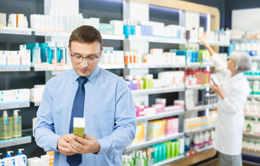 Man in glasses carefully chooses medicinal ointment in a pharmacy