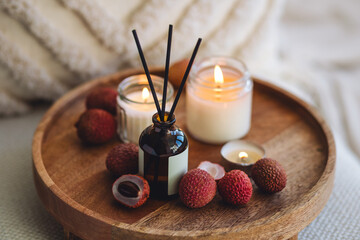 Sweet home perfume with tropical exotic fruits. Reed diffuser on wooden tray in a bedroom. Burning candles, atmosphere of relaxation, detention, meditation. Oriental interior, Bali, Thai vibes