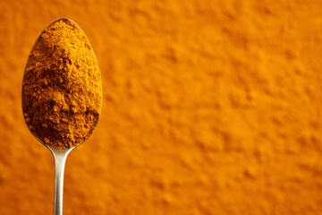 Turmeric root powder on a spoon on an empty background with copy space