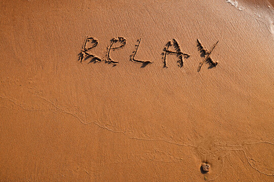 Hand drawn word Relax on wet yellow sand on beach of sea