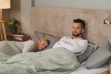 Young man deep in thoughts while his wife sleeps in the background 