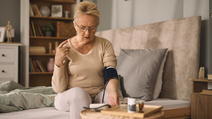 Elderly woman measuring blood pressure in bedroom