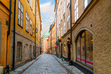 A narrow cobblestone alley of shops and cafes with Saint Gertrude German Church in view in the medieval old town of Gamla Stan island in Stockholm, Sweden.