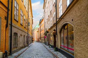 Papier Peint photo Lavable Ruelle étroite A narrow cobblestone alley of shops and cafes with Saint Gertrude German Church in view in the medieval old town of Gamla Stan island in Stockholm, Sweden.