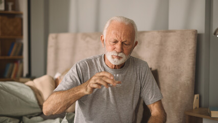 Elderly man drinking glass of water in bed