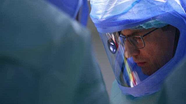 Caucasian surgeon in glasses and protective helmet. Face of a focused medic at operation. Close up.
