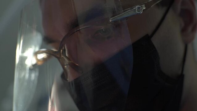 close-up shooting of a male face in a protective black mask and a plastic helmet, concentrated treatment of a tooth, focused unblinking gaze, arched eyebrows