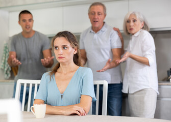 Domestic quarrel - offended young woman sits at the table while parents and young husband yell at...