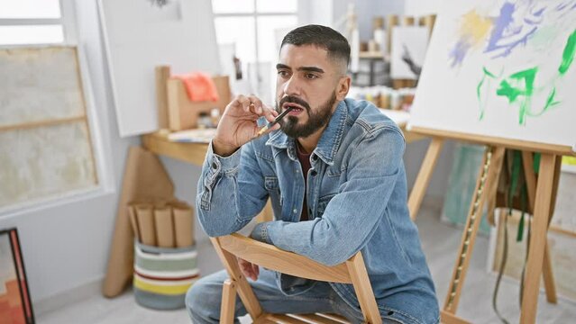 Bearded man contemplating while holding paintbrush in bright art studio