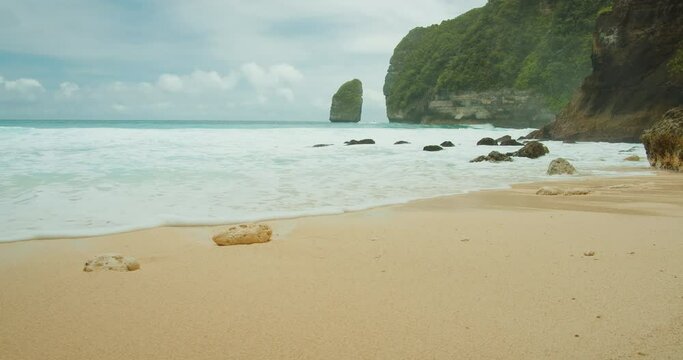 Close-up of serene beach with foamy waves and rocks. Tembeling, Nusa Penida, Bali, Indonesia.