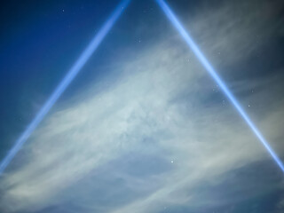 Blue spotlight beams form a triangle against a cloudy sky with stars at night. Copy Space
