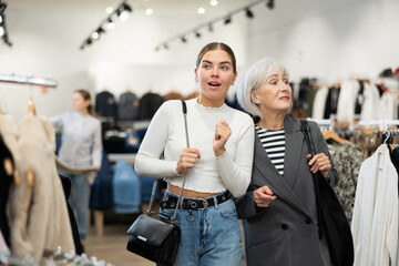 Two happy female customers looking around interestedly in large clothing store during shopping