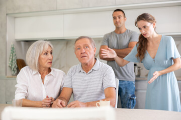 Couple of adult years man and woman sit in kitchen and quarrel with children