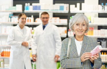 Fototapeta premium Elderly female shopper chooses a medicinal ointment in a pharmacy