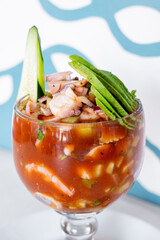 Mexican style seafood cocktail with shrimp, octopus, squid, tomato, tomato sauce and sauces, avocado, inside a seafood restaurant.