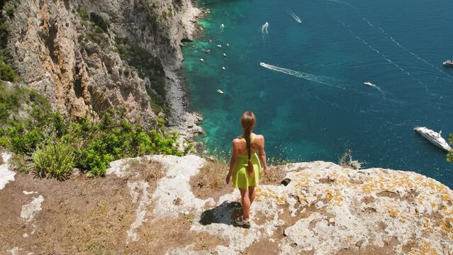 Hiker Gazing Down at the Crystal-Clear Coastal Waters from Above. Sheer cliffs drop to the emerald sea with boats on the water's surface. Capri, Italy.