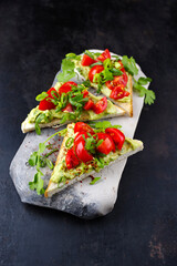 Traditional toast triangle sandwich with tomato, avocado spread and herbs served as a close-up on a grey design tray