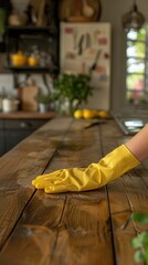A person wearing yellow rubber gloves is seen dusting a wooden table.
