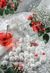 White meringues, zephyr, on lace napkin with cup of tea and rose flowers on light background. Sweets, dessert and pastry, homemade cakes, top view, selective focus