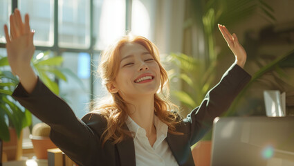 A businesswoman sitting in the office and raising his hands in joy with a laptop on his desk