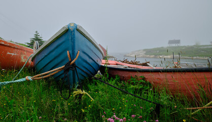 Colorful wood rowboats sit on dry land in the safety of Peggy's Cove Harbor Nova Scotia on a gray...